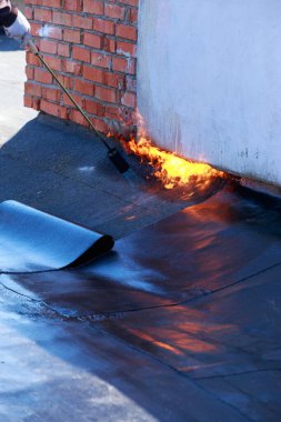 Çatı malzemelerinin arka planında ateş olan bir gaz yakıcı.