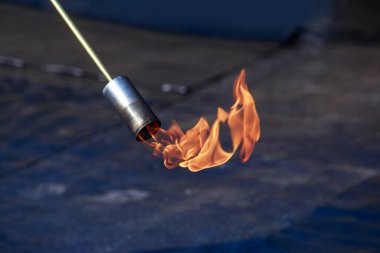 Çatı malzemelerinin arka planında ateş olan bir gaz yakıcı.