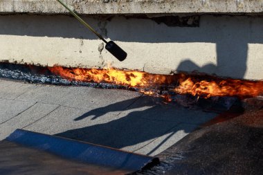 Çatı malzemelerinin arka planında ateş olan bir gaz yakıcı.