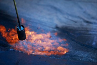 Çatı malzemelerinin arka planında ateş olan bir gaz yakıcı.