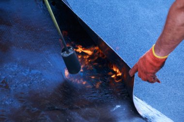 Çatı malzemelerinin arka planında ateş olan bir gaz yakıcı.