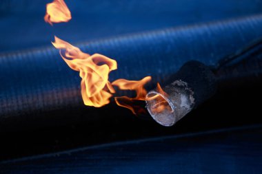 Çatı malzemelerinin arka planında ateş olan bir gaz yakıcı.