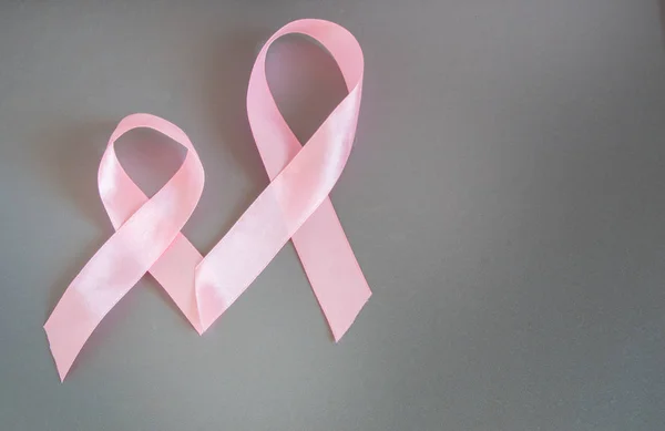 Two pink ribbons to raise awareness about breast cancer, the image on a gray background, copy space.