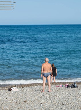 Yaşlı bir gri saçlı adam sahilde duran ve sertleştirme kavramı soğuk denizde yüzmek için hazırlanıyor ve sağlıklı yaşam tarzı
