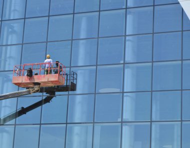 İşçi bir vinç platformunda ayakta, bir gökdelen cam cephesinde Windows yıkıyor