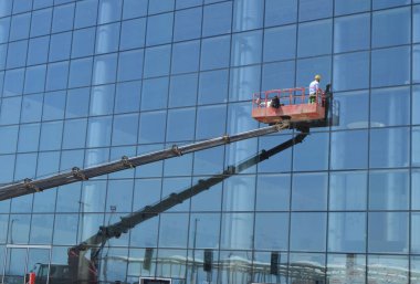 İşçi bir vinç platformunda ayakta, bir gökdelen cam cephesinde Windows yıkıyor