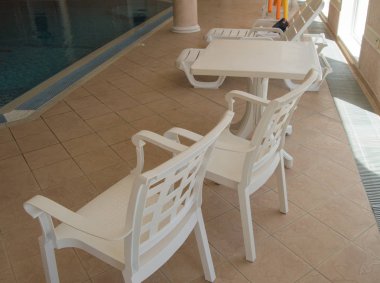 Rekreasyon alanı kapalı havuzun yanında beyaz plastik sandalyeler bulunmaktadır