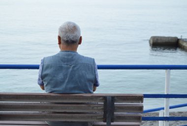 Oturan bir bankta deniz, arka görünümünden tarafından yalnız gri saçlı yaşlı adam