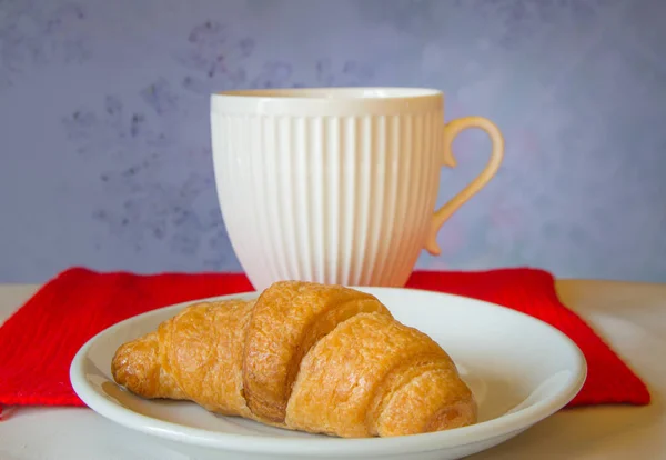 Vackra vita te kopp med en croissant på röd stickad halsduk — Stockfoto