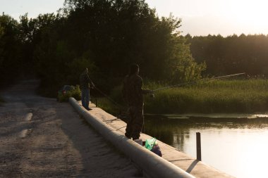 Sabahın erken saatlerinde gündoğumu, üzerinde parlak güneş ışığı ile bir olta balık tutma iki insan siluetleri