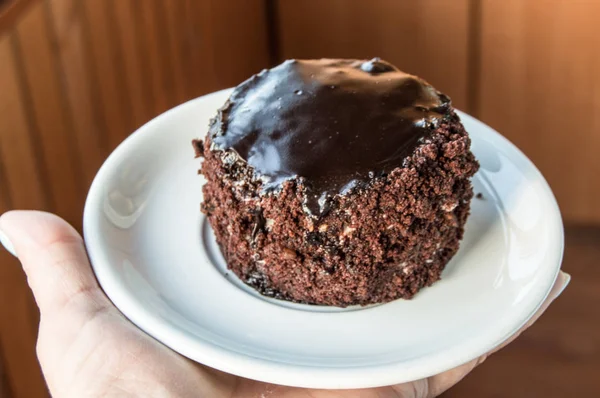 Шоколадный торт с глазурью лежит на тарелке, женская рука держит тарелку — стоковое фото