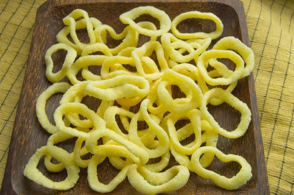 Deliziosi anelli croccanti di chip di cipolla si trovano su un piatto di legno scuro su uno sfondo di tovagliolo giallo — Foto Stock