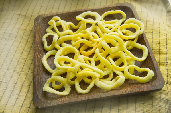Delicious crispy rings of onion chips lie on a dark wooden plate on a yellow napkin background — Stock Photo, Image