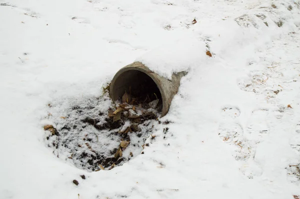Cemento alcantarillado tubería de drenaje, un agujero con hojas y tierra, cubierto con la primera nieve — Foto de Stock