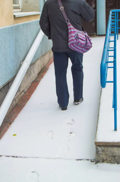 Un anciano enfermo de pelo gris sube con fuerza sobre una rampa cubierta de nieve para discapacitados, dejando rastros en la nieve —  Fotos de Stock