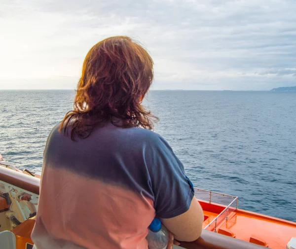 Ευτυχισμένη γυναίκα κοιτάζει την ακτογραμμή και τη θάλασσα, απολαμβάνοντας το ταξίδι κρουαζιερόπλοιων, τη θέα από πίσω — Φωτογραφία Αρχείου