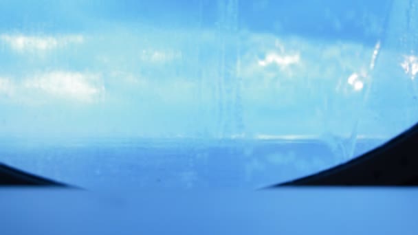 На стеклянном круглом иллюминаторе корабля течет вода, брызги от волн. Голубой фон — стоковое видео