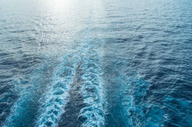 Mavi denizin yüzeyinde dalga ve köpük izleri ve günbatımında uzayın bir kopyası var.