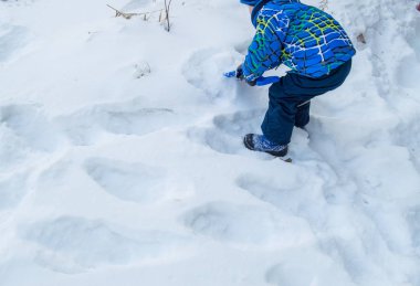 Çekici küçük oğlan kış günü kar mavisi kürek kazıyor..
