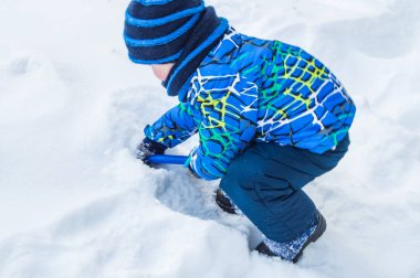 Çekici küçük oğlan kış günü kar mavisi kürek kazıyor..
