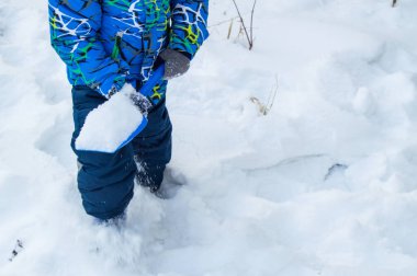 Çekici küçük oğlan kış günü kar mavisi kürek kazıyor..