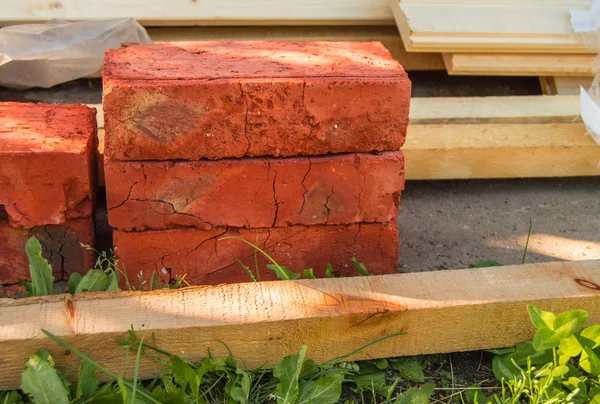 Building material for repairs in the garden-new red bricks, boards, lie on the grass.
