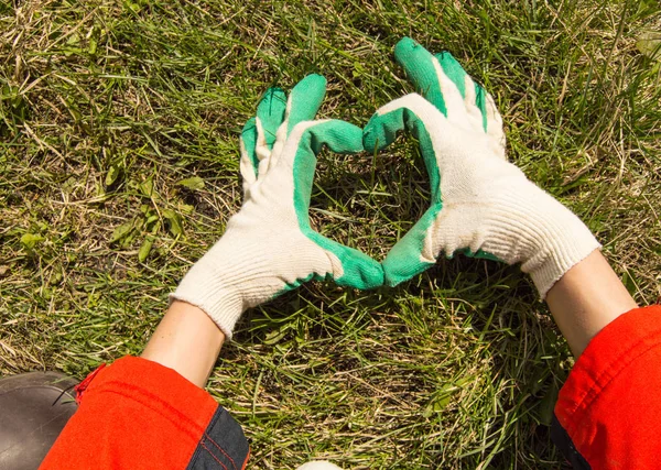 the concept of Earth Day, women\'s hands with gloves making a heart shape on a grass background, copy space.