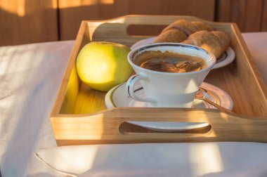 Lezzetli kahvaltı güneş ışığı altında kahve, balkonda kruvasan, Apple bir ahşap tepsi.