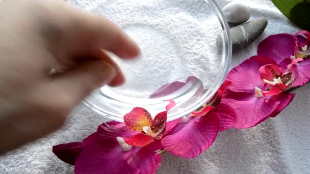 Kvinnlig hand förbereder vatten för en Spa-manikyr, en glasskål med vatten, en orkidé-gren och stenar — Stockvideo