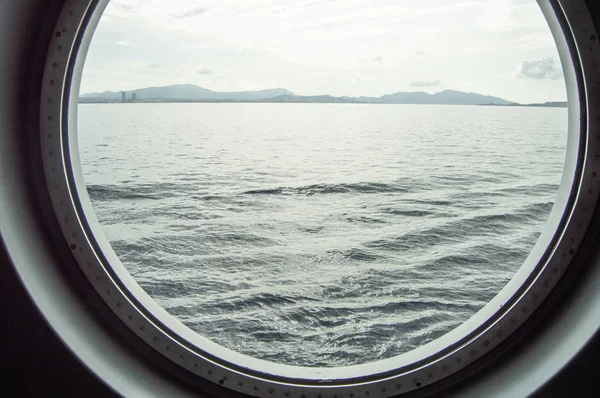 Στρογγυλή φινιστρίνι σε ένα κρουαζιερόπλοιο, εσωτερική θέα μέσα από το παράθυρο για την ακτή και τη θάλασσα, την ανατολή του ηλίου κατά τη θάλασσα, γκρο πλαν — Φωτογραφία Αρχείου