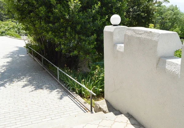 Sendero a pie con escalones en el Parque, a lo largo de una hermosa valla de piedra con plafones blancos, en verano —  Fotos de Stock