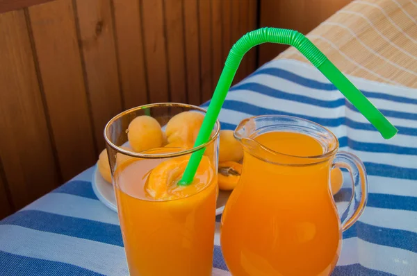 apricot juice in a glass with a straw and a glass pitcher