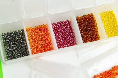 Fletley, yaratıcılık ve hobi için renkli boncuklu plastik kutu beyaz arka planda parlak boncuklar.