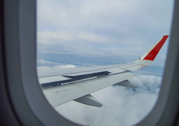 Skrzydło samolotu lecącego nad chmurami, widziane przez okno samolotu — Zdjęcie stockowe