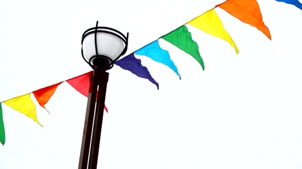 Coloridas banderas triangulares ondeando en el viento están atadas a un poste de luz. Decoración para vacaciones, al aire libre — Vídeos de Stock