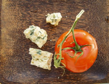 Tahta tabak, domates ve küflü peynir. Düz üst görünüm