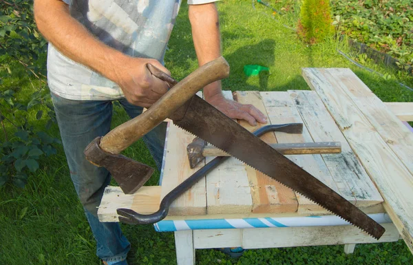 Hombre utiliza una sierra, un hacha, un martillo de garra para los trabajos de construcción en su jardín — Foto de Stock