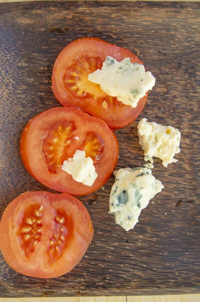 Italian culinary ingredients sliced tomatoes and cheese with mold on a dark rustic wooden plate