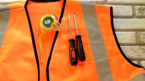 Na oranžovém stavebním vestě jsou nástroje pro konstrukci šroubováku, měřicí páska, klíč, koncept pracovní den — Stock video