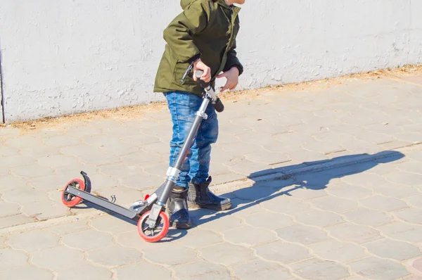 Niño adolescente montando un scooter en la ciudad, el NIÑO entra para los deportes en la primavera abierta —  Fotos de Stock