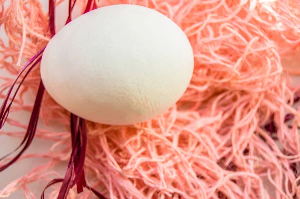 Пасхальная концепция, белое яйцо на розовом фоне, тканое гнездо, вид сверху, пространство для копирования, солнечный свет — стоковое фото