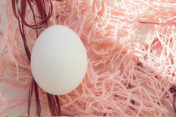 Пасхальная концепция, белое яйцо на розовом фоне, тканое гнездо, вид сверху, пространство для копирования, солнечный свет — стоковое фото