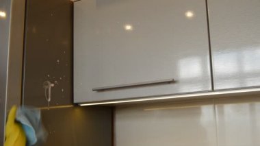 Sarı lastik eldivenli kadın eli, deterjan kullanarak buzdolabının ve mutfak dolabının yüzeyini temizliyor. Bahar temizliği ve ev işleri kavramı