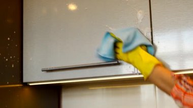 Sarı lastik eldivenli bir kadın eli modern plastik mutfak dolabının yüzeyini deterjan ve bezle temizliyor. Bahar temizliği ve ev işleri kavramı