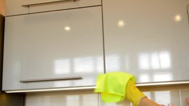 Sarı lastik eldivenli bir kadın eli modern plastik mutfak dolabının parlak yüzeyini bezle temizliyor. Bahar temizliği ve ev işi kavramı.