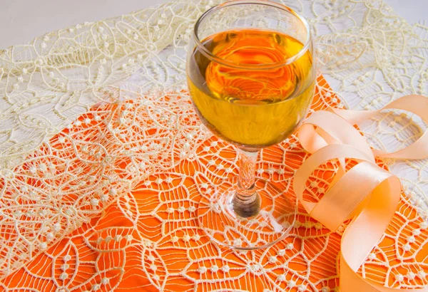 Empilement plat de vin blanc dans un verre, dentelle beige et ruban décoratif, fond orange, vue de dessus. Composition romantique printemps ou été — Photo