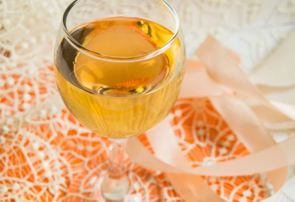 Плоская упаковка белого вина в бокал, бежевые кружева и декоративная лента, оранжевый фон, вид сверху. Романтическая весенняя или летняя композиция — стоковое фото
