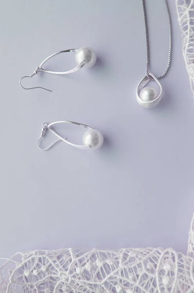 Красивые серебряные блестящие жемчужные украшения, модные гламурные серьги, цепь на тонком пастельном фоне с изысканным кружевом. Плоская, верхняя вертикальная рама — стоковое фото