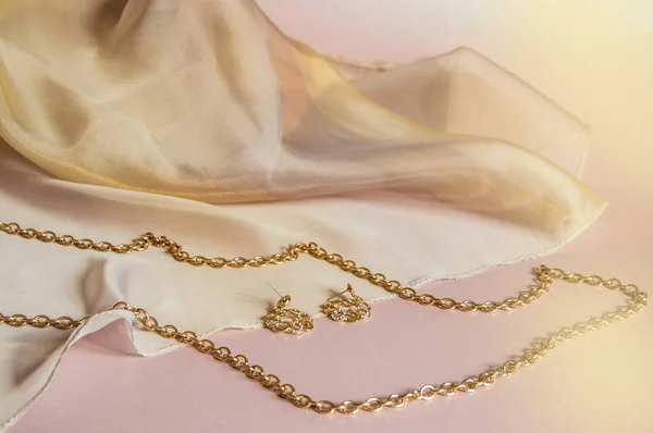 Роскошная золотая цепочка ювелирных изделий и серьги на розовом фоне с шелком, пространство для копирования, избирательный фокус — стоковое фото