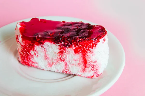 Gyönyörű puding torta vörösáfonya zselével, bogyós máz és kókusz egy fehér lemezen, közelről, rózsaszín háttér — Stock Fotó
